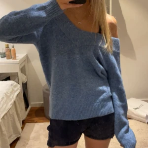 Blå offshoulder stickad tröja - Säljer denna blå stickade tröja med offshoulder-design och bred ribbad kant vid halsringning, ärmslut och nederkant. Gammal från hm så säljs inte längre. 