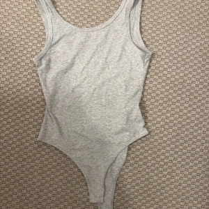 Grå ärmlös linnetopp - Säljer en enkel och stilren grå linnetopp i mjukt bomullsmaterial. Toppen är ärmlös med rundad hals och har en slim passform som sitter snyggt mot kroppen. Perfekt att styla med jeans eller kjol för en clean look.