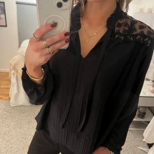 Svart blus med hjärtan och gulddetaljer - Tunn blus med svart spets i hjärtan över axlarna. Guldetaljer. Snören i kragen. Använder sällan, men mycket fin blus till middagar osv.☺️💖Vet ej märket då jag köpte den för ett tag sedan och klippte av lappen🫠 