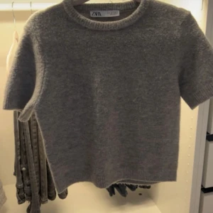 Grå stickad kortärmad tröja Zara - Mysig grå stickad tröja från Zara i storlek S. Tröjan har korta ärmar, rund halsringning och ribbade kanter. Perfekt för lager-på-lager och funkar året runt när du vill ha något enkelt men ändå stilrent.
