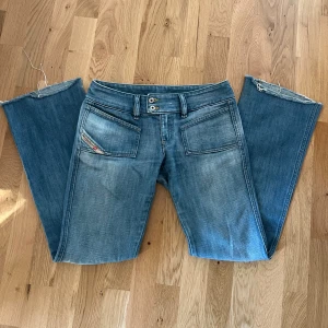 Blå bootcut jeans från Diesel - Snygga blå jeans från Diesel med bootcut passform och låg midja. Jeansen har två stora fickor fram, dubbla knappar i midjan och råa, fransiga benslut. Midjemåttet: 38cm Innerbenslängd: 76cm