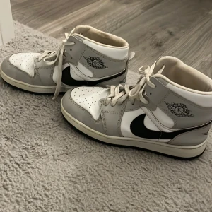 Nike Air Jordan 1 Mid grå/vit - Säljer ett par Nike Air Jordan 1 Mid, jättesnygga både killar och tjejer kan ha dessa skor passa fint på båda. Snygg färg och fina detaljer! skorna är vitfärgade med gråa och svarta detaljer. 