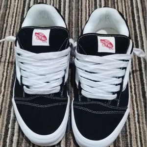 Svarta Vans Old Skool sneakers strl 45 - Säljer ett par klassiska Vans Old Skool sneakers i svart och vitt med den ikoniska sidoremsan. Skorna har vit platt sula, rund tå och breda vita snören. Materialet är en mix av mocka och canvas, med snygga kontrastsömmar och Vans-logga på plösen.
