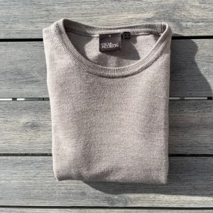 Beige stickad tröja Oscar Jacobson - Snygg beige stickad tröja från Oscar Jacobson. Klassisk rund halsringning och mjukt material som passar perfekt till lager-på-lager. Enkel och stilren design som funkar till många outfits.