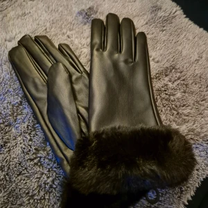 Svarta handskar med fuskpäls - Snygga svarta handskar  med mjuk och fluffig fuskpäls vid handleden. Handskarna har en stilren och klassisk design med slät yta och fem fingrar. Perfekta för kalla dagar när du vill hålla händerna varma och samtidigt se stilren ut.
