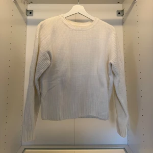 Vit ribbstickad tröja med rund hals - En stilren vit ribbstickad tröja med rund halsringning och långa ärmar. Tröjan har en klassisk passform och är perfekt för lager-på-lager. Mjuk och skön att bära under kyliga dagar.