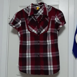 Rutig kortärmad skjorta från 365 Sunshine - Snygg rutig skjorta från 365 Sunshine i vinröda, vita och grå toner. Skjortan har korta ärmar, klassisk krage och knäppning framtill. Perfekt för dig som gillar en avslappnad men ändå trendig look.