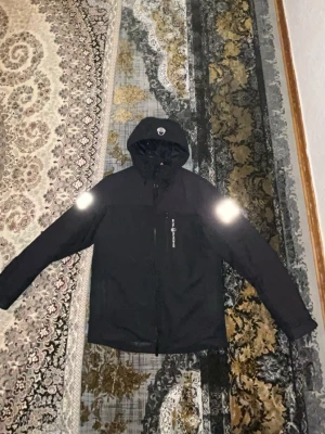 SAIL RACING (Jacka ny model) Helt ny utan skador ej använd - En helt ny SAIL RACING Jacka som är varm för vintern och helt unik i sitt slag. Svart vindjacka från Geographical Norway med huva, dragkedja framtill och bröstficka med logga. Jackan har reflexdetaljer på axlarna och tryck på ena ärmen. Perfekt för blåsiga dagar och snygg streetstil. Storlek M