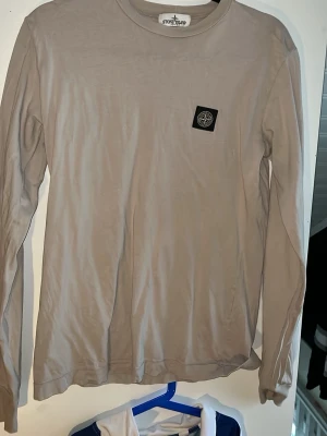 Beige långärmad sweatshirt  från Stone Island - Säljer denna snygga beigea långärmade sweatshirt  från Stone Island med klassisk rund hals och ikonisk logotyp-patch på bröstet. Tillverkad i mjuk bomull som känns skön mot huden. Perfekt för en stilren och avslappnad look. Tröjan är i storlek S och är varsamt använd fick den i julklapp för några år sedan och självklart äkta, ha de gött o hör gärna av er vid frågor!! 