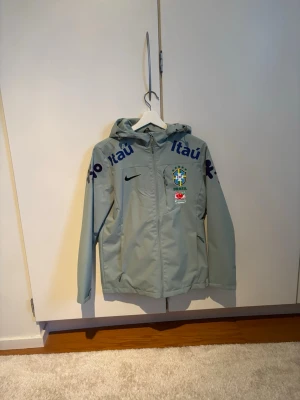 Brazil windbreaker träningsjacka - En riktigt snygg Brasilien windbreaker som är i helt nyskick, tafsen och allt medföljer, använd två gånger så i helt nyskick. Denna är också water resistent alltså vatten bara rinner av jackan vilket både är coolt och bra! Är M men passar även S