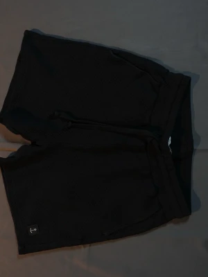 Svarta shorts från The Blue Uniform - Svarta shorts från The Blue Uniform med avslappnad passform och snörning i midjan. Tillverkade i ett mjukt, strukturerat material som känns skönt mot huden. Perfekta för varma dagar eller chill hemma.