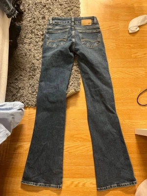 Mörkblå bootcut jeans med slitningar - Säljer ett par mörkblå bootcut jeans från 157 med stora slitningar på båda knäna. Jeansen har klassiska fem fickor och en snygg tvätt. Perfekta för dig som gillar en avslappnad och trendig stil.