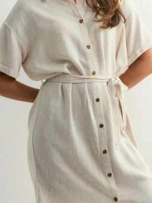 Beige skjortklänning med knappar - Stilren beige skjortklänning med knappar framtill och knytskärp i midjan. Klänningen har korta ärmar och en avslappnad passform, perfekt för varma dagar. Tillverkad i ett lätt och luftigt linnematerial.