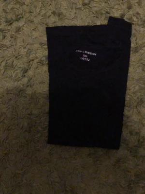 Svart topp från KappAhl - En enkel svart topp från KappAhl i storlek 152. Modellen är klassisk med korta ärmar och rund halsringning. Perfekt att matcha med jeans eller kjol för en clean look.