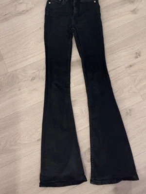 Svarta utsvängda jeans - Säljer ett par svarta jeans med hög midja och rejält utsvängda ben. Klassisk femficksmodell med knapp och dragkedja framtill. 