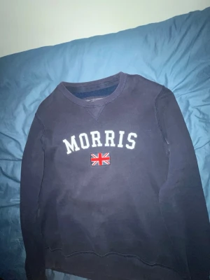 Mörkblå sweatshirt från Morris - Snygg mörkblå sweatshirt från Morris med vit broderad logga och brittisk flagga på bröstet. Klassisk rund halsringning och mjukt material som passar perfekt till jeans eller chinos.