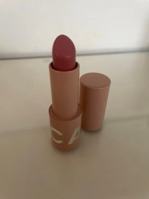 CAIA läppstift Britney's Fave rosa - Snyggt läppstift från CAIA i nyansen Britney's Fave. Färgen är en mjuk rosa ton och hylsan är stilren i matt beige plast med vit text. Läppstiftet har en klassisk form som gör det enkelt att applicera. Sparsamt använt