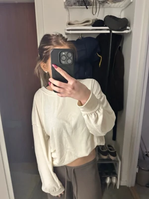 Vit croppad sweatshirt - En vit croppad sweatshirt med avslappnad passform och långa ärmar. Tröjan har rund halsringning och är tillverkad i ett mjukt material som känns skönt mot huden. Perfekt för en chill och trendig look.