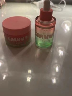 Smuuti Skin Watermelon Jelly & Serum - Säljer ett set från Smuuti Skin med Watermelon Jelly Cream i rosa/grön burk och Dew Serum i matchande glasflaska med pipett. Båda har en fräsch design med rosa lock och text. Perfekt för dig som vill boosta din hudvårdsrutin med fuktgivande produkter. Mer bilder finns att få
