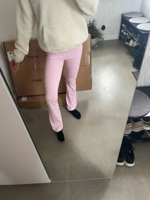 Ljusrosa leggings med bootcut - Snygga ljusrosa leggings med bootcut-snitt. De har en hög midja och är tillverkade i ett stretchigt material som sitter tight upptill och släpper ut vid bensluten. Perfekta för dig som vill ha en trendig och bekväm look.