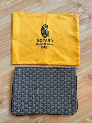 Svart Goy4rd kuvertväska med mönster - Snygg svart kuvertväska från Goy4rd med klassiskt vitt och grått mönster och silverfärgad dragkedja. Väskan är rektangulär och tillverkad i canvasmaterial. Perfekt för att bära det viktigaste och kommer med original dustbag.