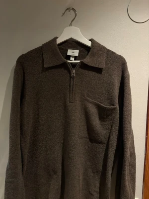 Brun stickad tröja med dragkedja H&M - Mysig brun stickad tröja från H&M med krage och halv dragkedja framtill. Tröjan har en liten bröstficka och långa ärmar. Perfekt för lager-på-lager och chill stil.