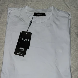Vit kortärmad t-shirt från BOSS - Säljer en stilren vit t-shirt från BOSS med diskret broderad logga på bröstet. Klassisk rund halsringning och korta ärmar. Tillverkad i mjuk bomull som känns skön mot huden. Perfekt till jeans eller shorts för en clean look. ( 2 stycken)