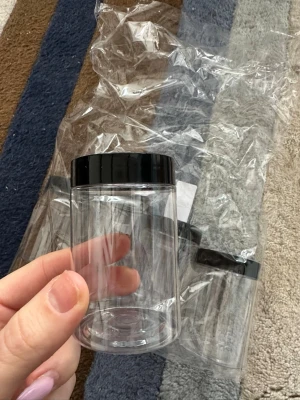 Tom genomskinlig burk med svart lock - Säljer fem lsmå runda och genomskinlig plastburk med svart skruvlock. Perfekt för att förvara smink, glitter, bomullspads eller andra små skönhetsprodukter. Enkel och stilren design som passar bra i necessären eller på sminkbordet.