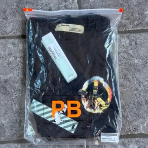 Off-White Rambo t-shirt - Säljer en svart t-shirt från Off-White med stor grafisk print på ryggen som visar en soldat, helikopter och texten 'MENS' samt 'SEEING THINGS' i blått. T-shirten har en avslappnad passform och är gjord i mjuk bomull. Perfekt för dig som gillar streetwear och unika prints.