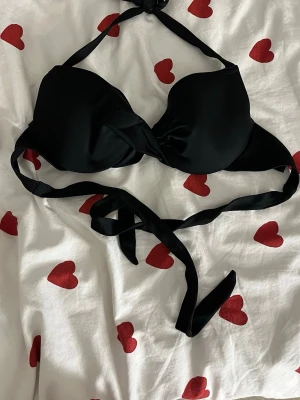 Svart bikiniöverdel med knytband - Snygg svart bikiniöverdel med vadderade kupor och knytband både i nacken och runt ryggen. Klassisk trekantsmodell som ger bra stöd och passar till många olika stilar. Perfekt för strand eller poolhäng.