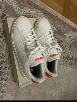 Helt Nya Adidas Advantage 2.0 Vita Sneakers – EU 40 ⅔ - Helt nya Adidas Advantage 2.0 sneakers i vitt med röd Adidas-logga baktill. Aldrig använda – helt oanvända. 	•	Märke: Adidas 	•	Modell: Advantage 2.0 	•	Färg: Vit med röda detaljer 	•	Storlek: EU 40 ⅔ / UK 7 / US 7.5 	•	Skick: Helt nya / Aldrig använda 	•	Originalkartong ingår.   #adidas #adidasadvantage #sneakers #trainers  #whitesneakers #unisex #newwithbox #neverworn  #adidasskor #vitaskor