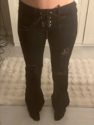 Svarta lace-up jeans Gina Tricot - Säljer ett par svarta jeans från Gina Tricot med snörning i midjan och slitna detaljer på benen. Modellen har utsvängda ben hoch coola hål vid knäna. Min kamera är sönder därav dålig kvalité Slutsålda! Skriv för frågor 
