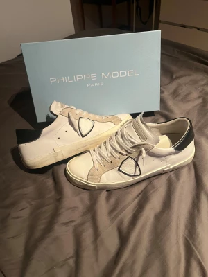 Philippe Model PRSX sneakers vit/svart - Snygga Philippe Model PRSX sneakers i vitt och svart med beige mockadetaljer och klassisk snörning. Skorna har en rund tå, platt sula och stilren design med logotyp på sidan. Materialet är skinn och mocka, vilket ger en lyxig känsla och cool look. Kvitto från merschsweden finns!