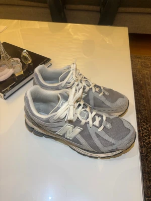 Grå New Balance sneakers med mesh - Säljer ett par grå New Balance sneakers med vit logga på sidan. Skorna har en chunky sula i svart och vitt, snörning och ventilerande meshpartier. De har rund tå och är tillverkade i syntet och mesh för extra komfort. Perfekta för dig som gillar sportig stil.