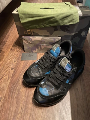 Valentino Rockrunner sneakers blå/svart - Säljer nu mina lätt fetaste skor i garderoben. Har haft dem i ca 2 är nu men det känns som dem har gjort sitt för mig. Köpta på Valentinos hemsida. Det finns lite slitage på plösen, storleks texten på plösen han nästan gått bort helt men syns fortfarande lite. Mockan är i okej skick och sulan har mycket liv kvar i sig. Kontakta mig vid frågor eller bud!