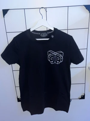 Svart Philipp Plein t-shirt med tryck - Svart t-shirt från Philipp Plein med coolt grafiskt tryck på bröstet och stor röd döskalle med text på ryggen. Rund hals och korta ärmar. Materialet är mjuk bomull och designen har vita och röda detaljer som sticker ut.