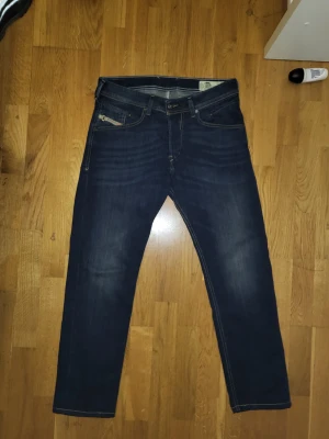 Mörkblå diesel jeans W30 L32 - Säljer ett par mörkblå  jeans med snygga slitningar och klassiska fem fickor. Jeansen har en smal passform och är tillverkade i stretchigt denim för extra komfort. Perfekta för dig som gillar en modern och stilren look. W30 L32 