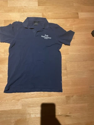 Mörkblå Peak Performance piké storlek 160 barnstorlek  - Säljer en klassisk mörkblå pikétröja från Peak Performance med vit broderad logga på bröstet. Tröjan har krage, korta ärmar och knäppning framtill. Perfekt för en sportig och stilren look.