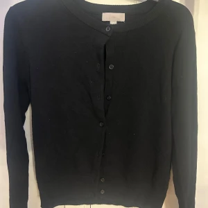 Svart kofta från H&M i storlek S - En klassisk svart kofta från H&M med rund halsringning och knäppning framtill. Koftan har långa ärmar och är tillverkad i ett mjukt, stickat material som passar perfekt till lager-på-lager-stil.