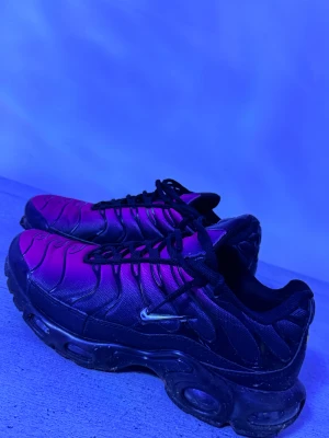 Nike sneakers svart/lila EUR 41 - Nike sneakers med unik svart och lila färgskiftning, coola vågformade detaljer på ovansidan och klassisk Swoosh på sidan. Skorna har snörning och en chunky platt sula med synliga luftkuddar. Materialet är syntet och mesh för skön komfort och streetstil.