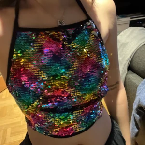 Paljett halterneck topp med öppen rygg - Reversibel topp med en sida regnbågspaljetter och en med silver. Passar bra till nyår eller fest! Köpt på beyond retro för en herrans massa år sedan men kommer inte till användning. Står M/L på lappen men passar mig med XS/S. Justerbar med band i nacken och bak i ryggen.