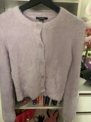 Ljuslila fluffig kofta från Esmara - Supermjuk och fluffig ljuslila kofta från Esmara i storlek XS. Koftan har rund hals, långa ärmar och stängs med matchande knappar framtill. Perfekt för dig som vill ha en cozy och trendig look.