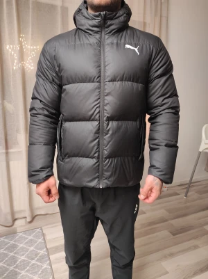 Svart pufferjacka från Puma - Säljer en svart pufferjacka från Puma med stor logga på ryggen och mindre logga på bröstet. Jackan har huva, dragkedja framtill och två sidofickor. Perfekt för kalla dagar och riktigt snygg streetstil.