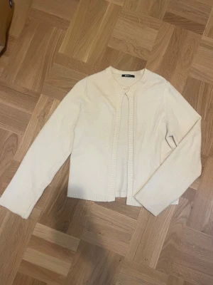 Beige kofta från Gina Tricot - Snygg beige kofta från Gina Tricot med rund hals och lång ärm. Koftan har en enkel knapp framtill och ribbade kanter vid hals, ärmslut och nederkant. 