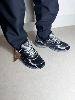 Svarta och grå Asics sneakers med dubbla snören  - Säljer ett par snygga Asics sneakers i svart och grått med vita detaljer. Skorna har meshpaneler för extra ventilation, klassisk snörning och en robust platt sula. Perfekt för dig som gillar sportig stil och vill ha bekväma skor med cool design. Skorna har dubbl snören. Storlek 42,43,43.5,44