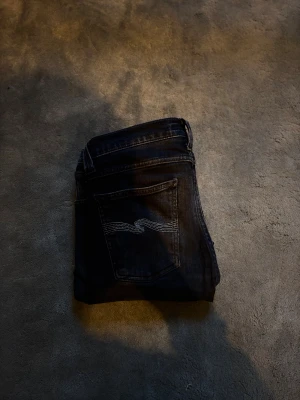 Mörkblå jeans med broderad bakficka - Snygga svarta jeans med klassisk femficksdesign och en broderad våg på bakfickan. Jeansen har raka ben och normal passform, perfekta till en skön tröja eller liknande! 