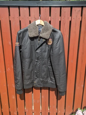 Vaxad bomull, jacka, slim M, svart, Hampton Republic - Svart vinterjacka i vaxad bomull från Kappahls märke Hampton Republic. I mycket gott skick. Storlek är S men skulle lika gärna kunna vara en slim M. Ordinarie pris 1200 kr.  Bröstmått (armhåla till armhåla): 110 cm Längd (krage till fåll): 70 cm.  Vid frågor kontakta mig gärna via chatt eller epost.