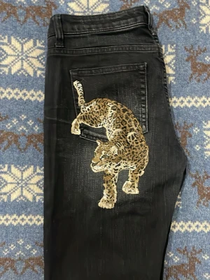 Svarta Acne Jeans med leopardbroderi - Unika svarta jeans från Acne Jeans med coolt leopardbroderi på bakfickan. Jeansen har en straight passform, klassiska fem fickor och snygga slitningar framtill. Materialet är jeans och färgen är mörk med ljusa detaljer. Perfekt för dig som vill sticka ut med din stil.