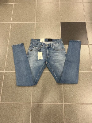 Ljusblå slimmade jeans från Tiger of sweden W29 L32 - Snygga ljusblå slimmade jeans från T/J med klassisk femficksdesign, smal passform och smala ben. Jeansen har en brun patch med logga bak i midjan och är tillverkade i stretchig denim för extra komfort. Perfekta för dig som gillar en slimmad look.