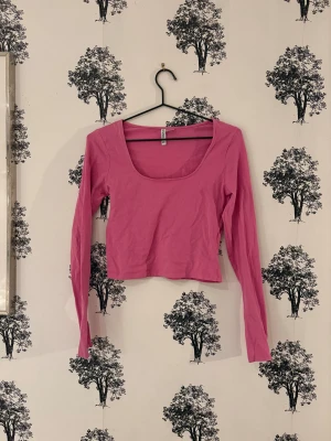 Rosa croppad långärmad topp H&M - Säljer en rosa croppad topp från H&M med lång ärm och djup rundad halsringning. Enkel och clean design, perfekt att styla med jeans eller kjol. Materialet är mjuk bomull som känns skönt mot huden. Basic-plagg med snygg passform och fräsch färg.